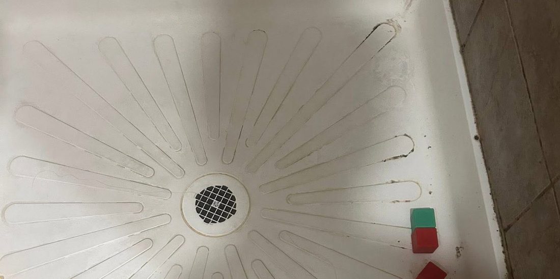 A shower pan with staining and debris before cleaning