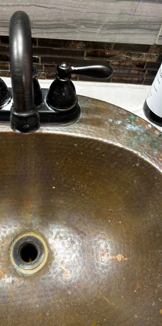A copper basin dulled by heavy mineral and soap build-up before cleaning